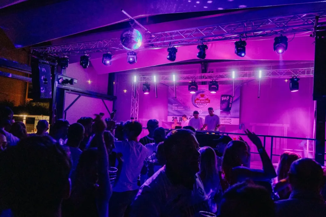 Beleuchtete Bühne bei Nachtparty, DJ und tanzendes Publikum in lila Licht.