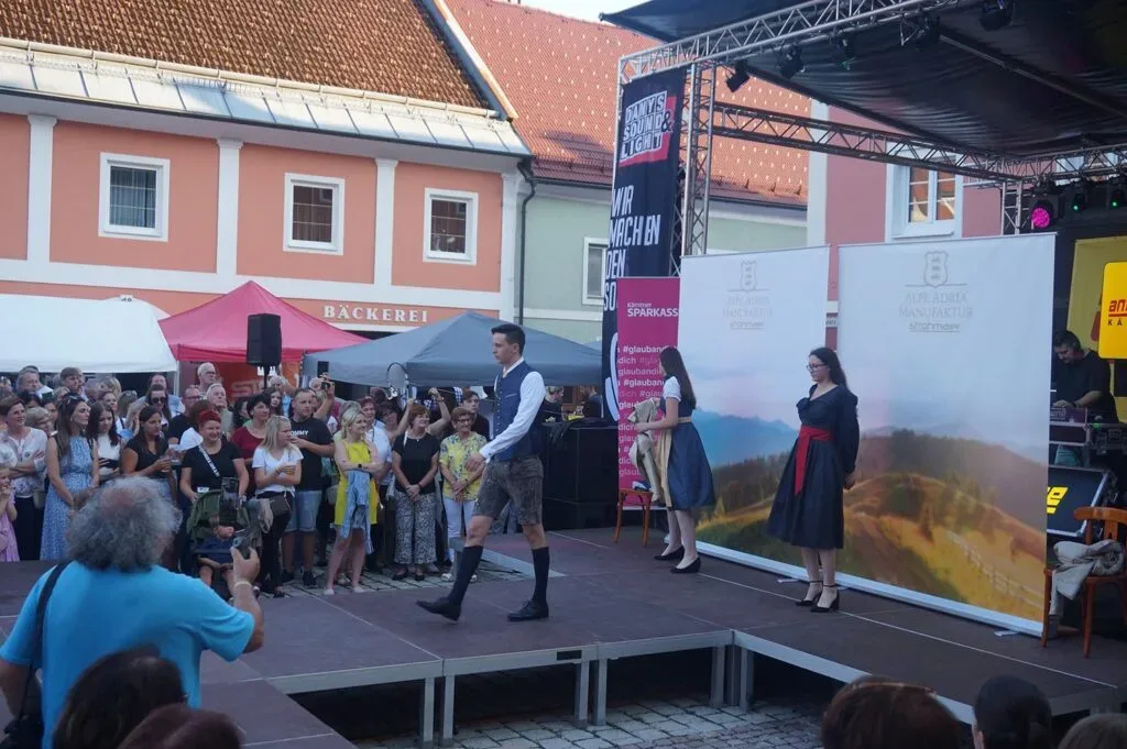 Modenschau im Freien mit traditionellen Trachten vor einem großen Publikum.