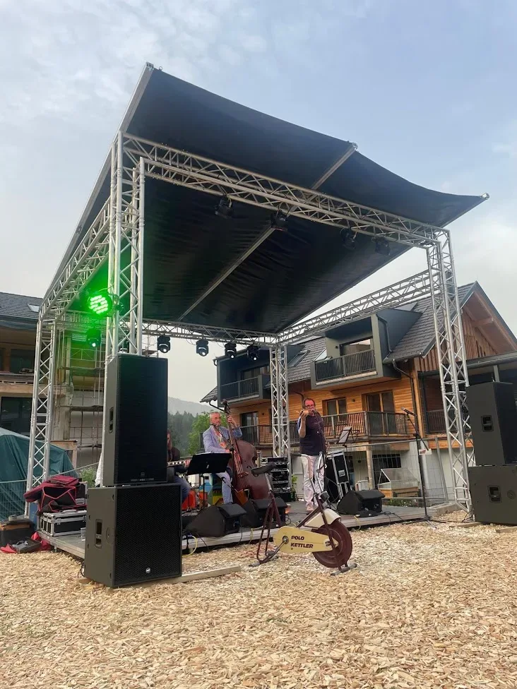 Open-Air-Bühne mit Musikern und Lichttechnik vor Holzgebäuden.