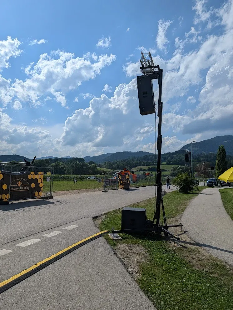 Lautsprecheranlage auf einer Landstraße vor einer Bergkulisse unter teils bewölktem Himmel.